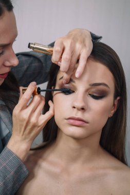 Makyaj sanatçısı güzel bir genç kız için yüz ifadesi yapıyor, maskarayı göz olarak kullanıyor. Makyaj, makyaj, güzellik standartları, cilt bakımı konsepti. Yakın çekim..