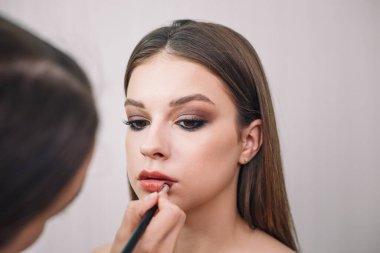 Dudak boyası kullanarak genç ve güzel bir kız için makyaj sanatçısı. Makyaj, makyaj, güzellik standartları, cilt bakımı konsepti. Yakın çekim..