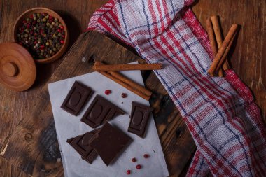 Kırık, acı çikolatalı, biberli, tarçınlı, kırmızı biberli kağıt üzerinde, ahşap arka planda. Alışılmadık tat