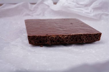 Beyaz kağıtta gözenekli çikolata. Kabarcıklı ya da süngerimsi çikolata, lezzetli tatlılar, karbonhidratlı yiyecekler, tatlı cazibe, sağlıksız beslenme