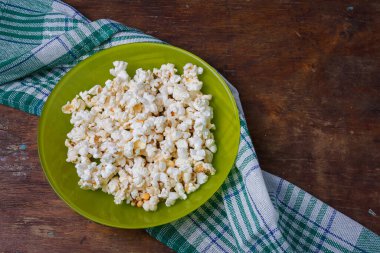 Mutfak havlusuyla ahşap masa arkasında yeşil tuzlu patlamış mısır tabağı. Üst görünüm, alanı kopyala