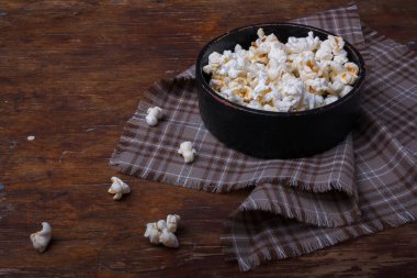 Tahta kırsal arka planda siyah kasede patlamış mısır yığını. Kumaş ve masada patlamış mısır.