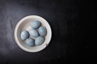 Paskalya yumurtaları siyah ahşap arka planda beyaz kâseye maviye boyanmış. Üst görünüm, alanı kopyala