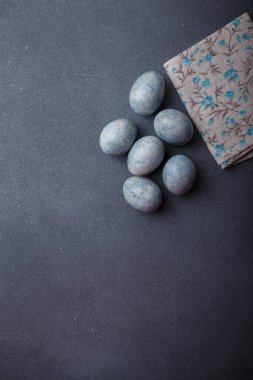 Paskalya yumurtaları gri ahşap arka planda mutfak havlusuyla maviye boyandı. Üst görünüm, kopyalama alanı, dikey çekim