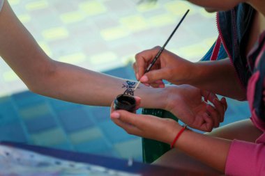 Kınalı resim yapan bir kadın, bileğine geçici dövme çiziyor. Kınalı boya kullanıyor.