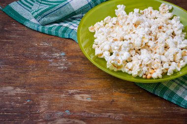 Ahşap masa arkasında yeşil mutfak havlusuyla patlamış mısır tabağı. Yakın çekim, boşluğu kopyala
