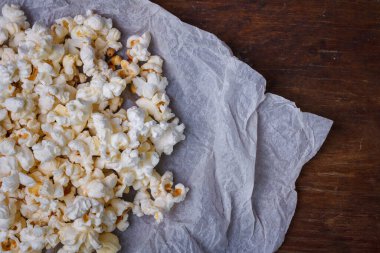 Beyaz kağıt üzerinde tuzlanmış patlamış mısır yığını. Kahverengi masa arkası, yakın çekim.