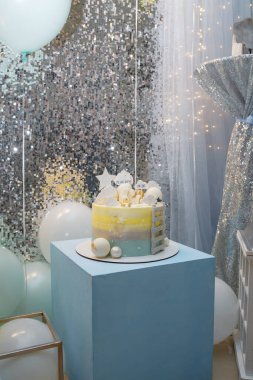 Mavi küpün üzerinde duran 1 yaşındaki çocuk doğum günü pastası. Bulutlar, bebeğin kilosu ve tarihiyle yıldız üstleri, pastanın üstünde oyuncak ayı. Dikey çekim