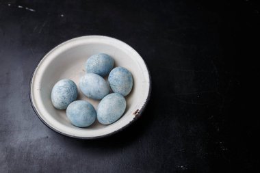 Paskalya yumurtaları siyah ahşap arka planda beyaz kâseye maviye boyanmış. Boşluğu kopyala