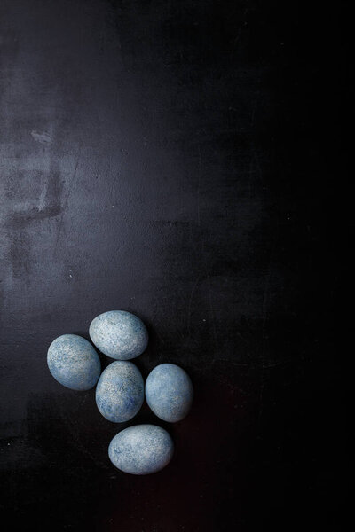 Easter eggs painted blue on black wooden background. Top view, copy space, vertical shot