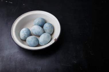 Paskalya yumurtaları siyah ahşap arka planda beyaz kâseye maviye boyanmış. Boşluğu kopyala