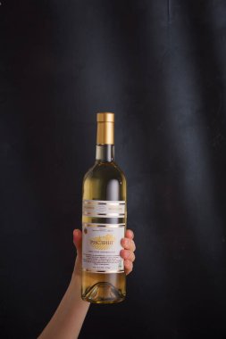 İzmail, Ukrayna. Kasım 2022. Besarabian şaraphanesi. El ele tutuşan beyaz şarap şişesi Riesling. Siyah arkaplanda alkol içeceği