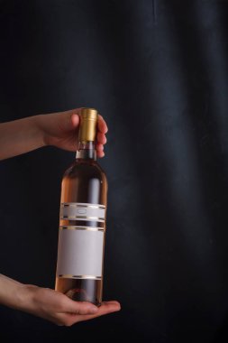 Elinde sahte etiketli pembe şarap şişesi olan eller, siyah arka planda marka yok. pinot noir. Alkol içeceği, kopyalama alanı
