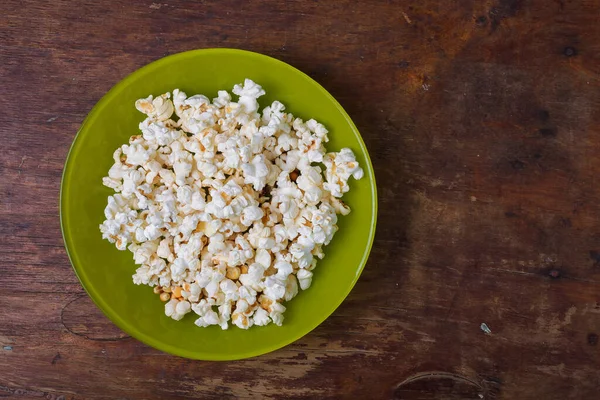 Ahşap masa arkasında yeşil tuzlu patlamış mısır tabağı. Üst görünüm, alanı kopyala