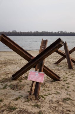 Çek tanksavar kirpileri ve nehir kıyısında uyarı levhası. Kumda tanksavar engelleri var. Rus saldırısına karşı Ukrayna 'nın savunma savaşı