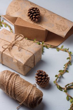 Kraft kağıdına sarılı, jüt halat ve kozalaklı Noel hediyesi kutusu. Doğal dekoratif elementler, toprak tonlu, plastik yok.