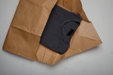 Gri pamuklu tişört beyaz arka planda doğal kağıt paketi. Çevre dostu ürün ambalajı. Çevreye dikkat et