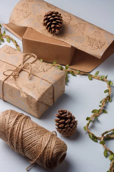 Kraft kağıdına sarılı, jüt halat ve kozalaklı Noel hediyesi kutusu. Doğal dekoratif elementler, toprak tonlu, plastik yok.