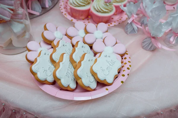 女婴一岁生日糖果棒 粉红色和白色姜饼 花朵形状 上面有名字题词 背景的棉花糖和纸杯蛋糕 — 图库照片