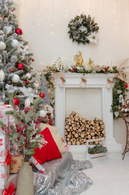Mutlu Noel dekoratif şöminesi içinde ahşap kütükler, kırmızı ve beyaz ampullü köknar ağacı, duvarında çelenk. Şenlikli oturma odası
