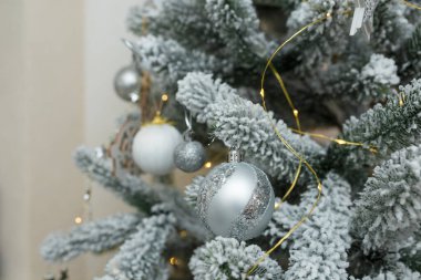Yapay karla kaplı köknar ağacı dalları, beyaz ve gümüş ampuller, mücevherler, altın çelenkler. Noel ağacı yakın plan