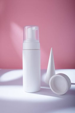 Pembe arka planda beyaz şişe, marka şablonu yok. Beton dekoratif elementlerle köpük kabı temizleniyor