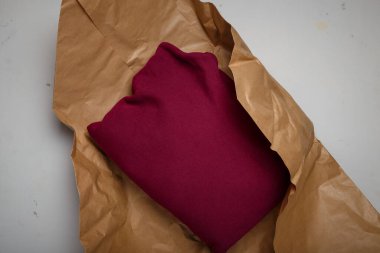 Beyaz arka planda doğal kağıt paketin içinde bordo pamuklu kapüşonlu kapüşon. Çevre dostu ürün ambalajı. Çevreye dikkat et