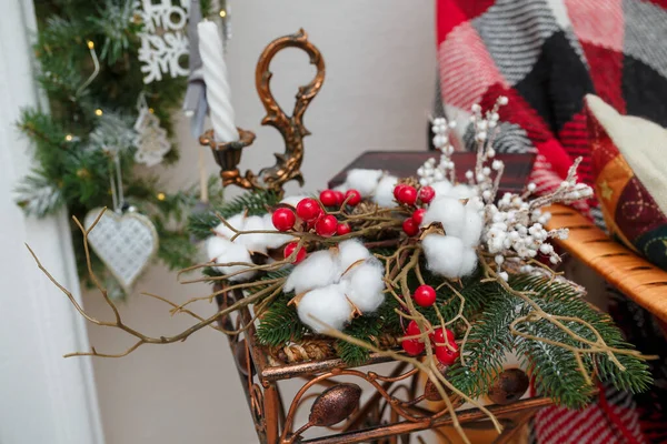 クリスマスの花構成 モミの枝からの花束 赤い果実と白い綿の花 キャンドルスティックでキャンドルスティック バックグラウンドでソファで遊ぶ — ストック写真