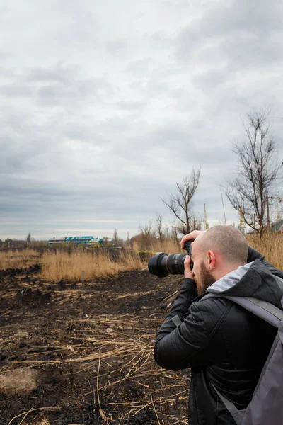 journalist or photographer making captures of dramatic landscape of lake with burnt reeds after natural fire