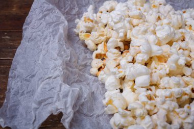 Beyaz kağıt üzerinde tuzlanmış patlamış mısır yığını. Kahverengi masa arkası, yakın çekim.