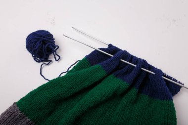 Örgü örme, aksesuar yapımı. Örgü iğneleri ve iplik yumağı, beyaz arka planda iplik. Çizgili mavi, yeşil, gri kumaş