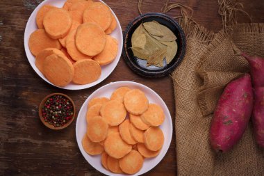 Çuval bezelyeli mor çiğ patates, tabakta portakallı tatlı patates, ahşap rustik masa, bütün baharatlı bezelyeler, defne yaprakları. Çiftlik hasadı, organik sebzeler, yerel alışveriş