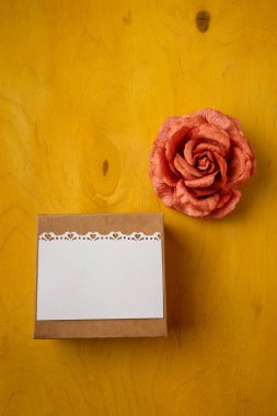 İçinde beyaz kartpostal olan mevcut kutu, parlak sarı arka planda kumaş gül, üst manzara, kopyalama alanı. Doğum günü, düğün, anneler, Sevgililer Günü