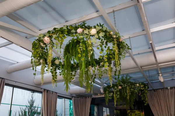 Circle on ceiling decorated with hanging green plants, foliage and rose flowers. decorative chandeliers with greenery