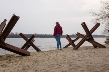 Nehir kıyısındaki anti-tank czech kirpilerinin arasında Ukraynalı bir adam. Rus askeri saldırısını, savaş istilasını ve 2022 Ukrayna 'daki soykırımı durdurun.