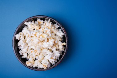 Parlak mavi arka planda siyah kasede patlamış mısır yığını. Üst görünüm, alanı kopyala.