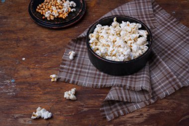 Tahta kırsal arka planda siyah kasede hazır ve çiğ patlamış mısır yığını. Kumaş ve masada patlamış mısır.