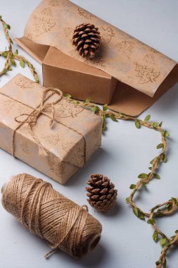 Kraft kağıdına sarılı, jüt halat ve kozalaklı Noel hediyesi kutusu. Doğal dekoratif elementler, toprak tonlu, plastik yok.