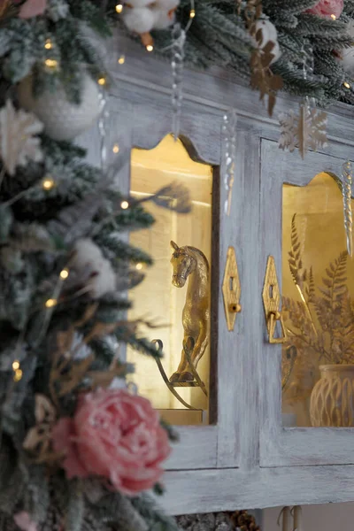 雪のモミの枝や氷のバラ 雪のフレークや自転車で飾られた食器棚のガラスの後ろに黄金のロッキング馬のおもちゃ — ストック写真