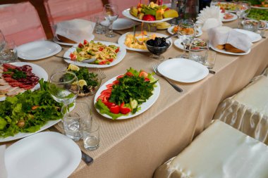 Festive table with appetizers. Fruit plate, vegetable salads. Herring with lemon and greenery. Cheese plate with honey and prunes. Empty glasses, plates for guests
