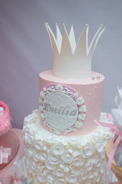 Girlish birthday cake. Pink dessert with mastic crown shape, white cream roses flowers and inscription name Emilia. Cake for 1 or 5 years old girl