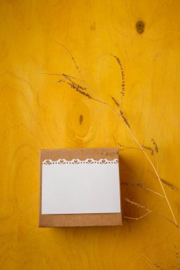 Present box with blank white postcard, branch on bright yellow background, top view, copy space. Birthday, wedding, mothers, Valentines day