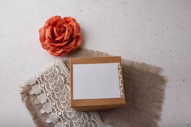 Brown paper present box, fabric rose flower, blank postcard, sackcloth and lace on white background. Valentines day, birthday, wedding