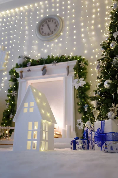 Decorative fireplace with candles and wood, wrapped present boxes under Christmas tree with baubles and garland. WInter holidays