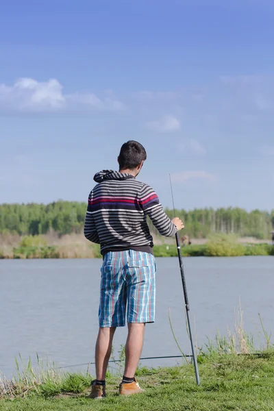 Young man with a fishing rod on the river bank — Stock Photo, Image