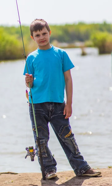 Niño con una caña de pescar en la orilla del río — Foto de Stock