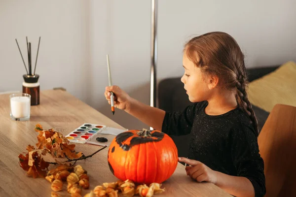 Küçük bir kız Cadılar Bayramı için bir odada balkabağı süslüyor. Çocuklar evi dekore eder. Çocuklar balkabağı oyar. Ürkütücü Cadılar Bayramı eğlencesi