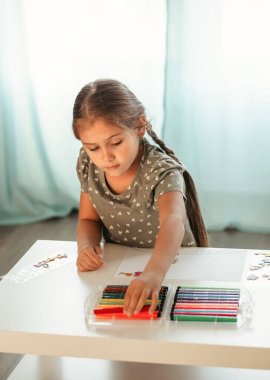 Küçük bir kız renkli kalemlerle resim çiziyor.