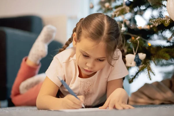 小さな子供の女の子は屋内でギフトの背景の新年の木の手紙サンタクロースと夢を書いています メリークリスマスとハッピーホリデー — ストック写真