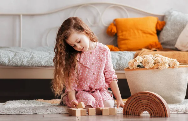 Plastik olmayan tahta oyuncaklar konsepti. Güzel küçük kız çocuk odasında tahta oyuncakla oynuyor.